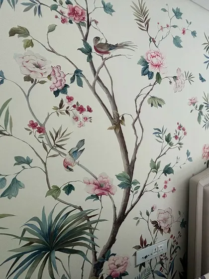 A bedroom sanctuary is created with this hand-painted Chinoiserie wallpaper. The design features delicate birds perched on blossoming branches, offering a unique blend of color, texture, and artistry that elevates the entire room.