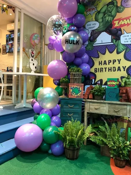 A powerful Hulk-themed birthday setup. This decoration features a comic-book style backdrop, green and purple balloons, and themed props to make any superhero fan's day.