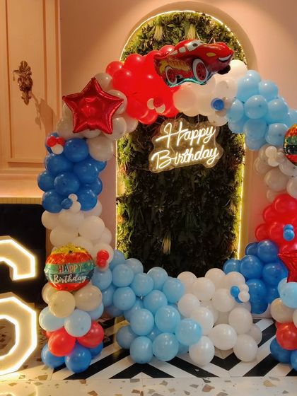 For a fan of Disney's Cars, this Lightning McQueen themed party is a winner. The setup includes a balloon arch in red, white, and blue, a large marquee number '6', a neon birthday sign, and a prominent Lightning McQueen foil balloon at the top.