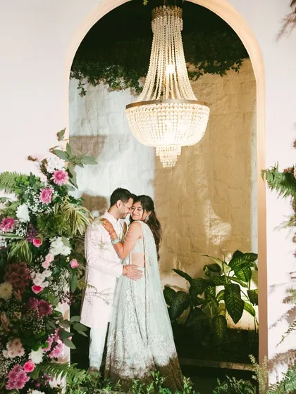 Framed by a floral arch and a magnificent chandelier, Avi and Devika share a quiet moment during their engagement celebration. I love blending grand decor with genuine emotion to create portraits that feel both opulent and authentic.