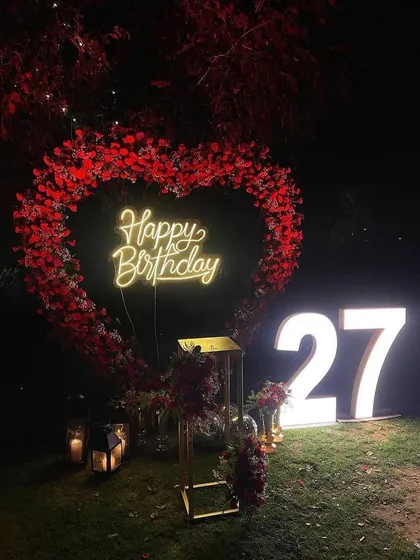 This image captures the full ambiance of the heart-shaped floral arch at night. The combination of the glowing neon sign and surrounding lanterns creates a truly magical setting in the garden.