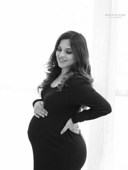A close-up black and white shot, capturing a gentle smile and the loving way a mother holds her bump. It's a quiet, beautiful moment.