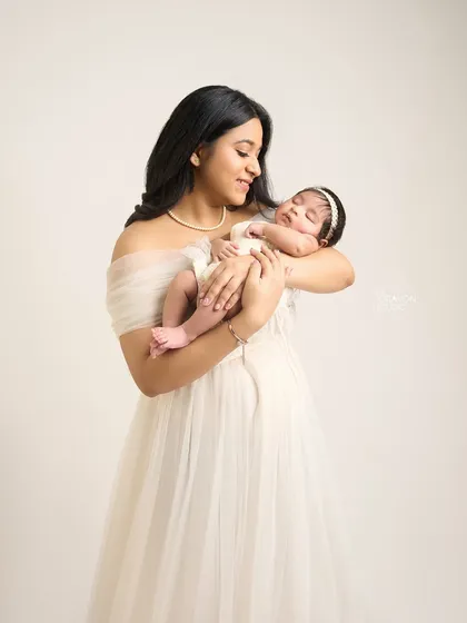 A mother gazes lovingly at her sleeping baby, her expression a mix of awe and adoration. The soft studio light enhances the gentle, peaceful mood.