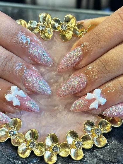 Stiletto nails with a pink glitter ombre effect, accented with 3D white bows for a cute and sparkling finish.