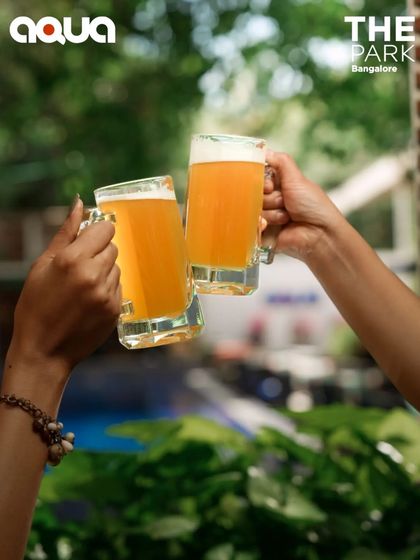 Cheers to good times and great beer! Friends toasting with mugs of our craft beer at Aqua, enjoying the lush, green surroundings.