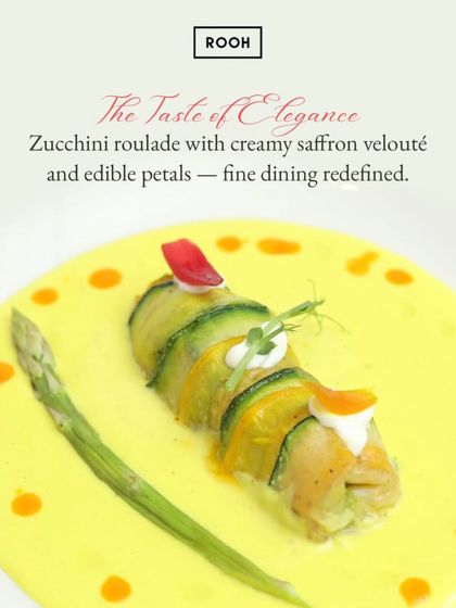 The Taste of Elegance: a delicate zucchini roulade filled with a savory stuffing, served with a creamy saffron velouté and edible petals. This dish redefines fine dining with its grace and flavour.