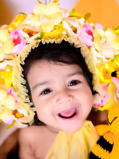 A close-up of a smiling baby girl in a honeybee-themed floral bonnet.