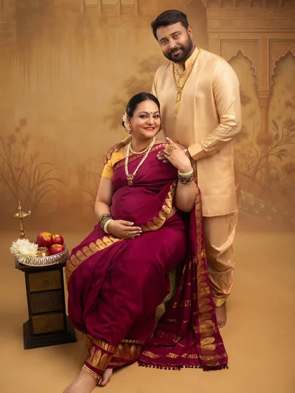 A classic seated portrait of the couple. The rich maroon saree and traditional jewelry, paired with the husband's kurta, create an image of timeless elegance and togetherness.