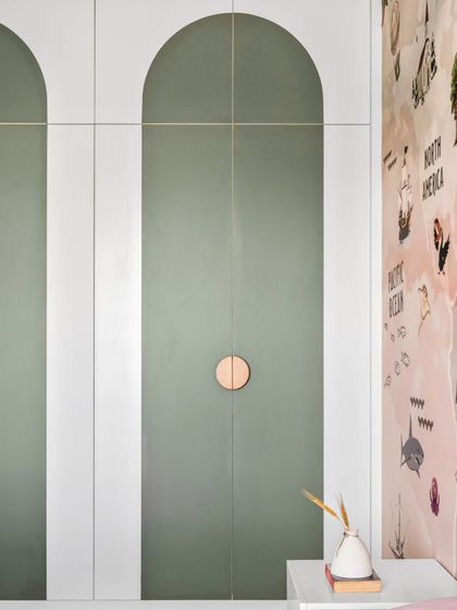 A detail of the custom wardrobe in the kids' room. The doors feature a modern arched design in a soft olive green, with simple circular wooden knobs that are easy for little hands to use.