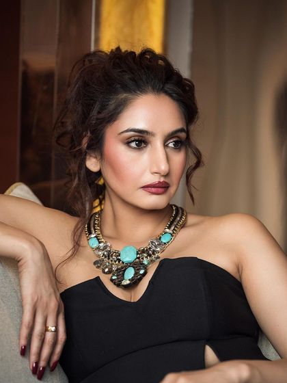 A classic, elegant portrait focusing on the subject's expression and a bold statement necklace. The soft lighting and relaxed pose create a look of authentic, effortless glamour.