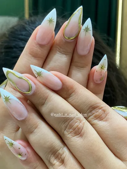 A celestial-themed design on long stiletto nails. This look features a soft ombre base, gold chrome outlines, and hand-painted gold stars for a magical, sparkling finish.