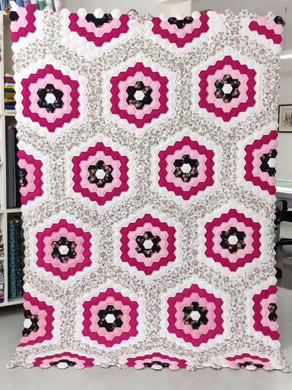 A stunning hexagon quilt in shades of pink and black, with a scalloped edge.