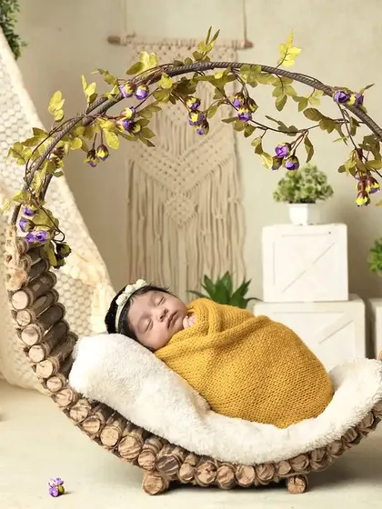 A newborn rests peacefully in a rustic, circular wooden prop adorned with leaves and flowers, showcasing a natural and earthy style of newborn photography.