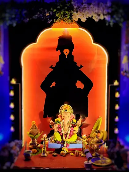 A beautifully composed shot of a Ganesh idol with a backlit silhouette of Lord Vitthal. The warm orange and cool blue tones create a stunning contrast, highlighting the intricate decoration.