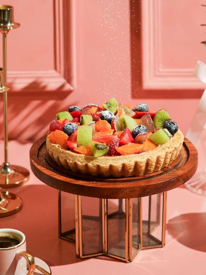 A light dusting of powdered sugar falls on our vibrant fresh fruit tart, adding a touch of magic.