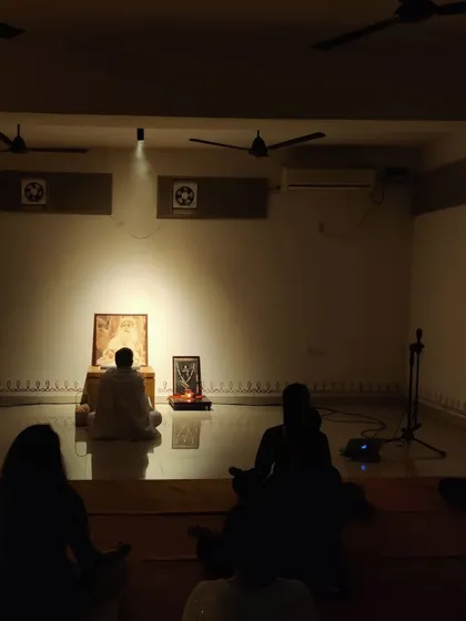 A wide view of the hall during a Sadhguru Sanidhi process. The room is filled with people sitting in stillness, their focus on the Guru's presence at the front.