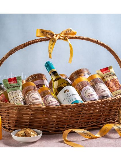 A beautifully arranged gift basket with wine and a variety of snacks, tied with a branded ribbon.