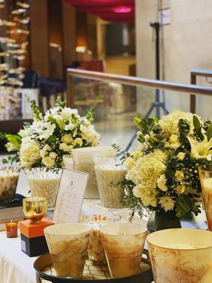 For this display table, I created two matching bouquets with white flowers and fresh greens to complement the products. Using multiple smaller arrangements can be just as effective as one large one for events or pop-up stalls.