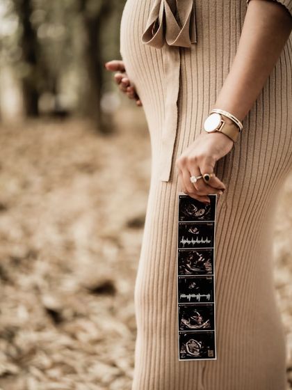 A close-up on the baby bump with the sonogram pictures held beside it. This shot, set against the autumn leaves, beautifully connects the new life with the cycles of nature.