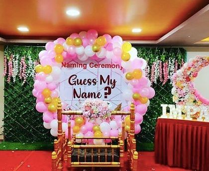 A fun and interactive naming ceremony setup. A large balloon wreath frames the "Guess My Name?" sign, with a traditional cradle placed in the center.
