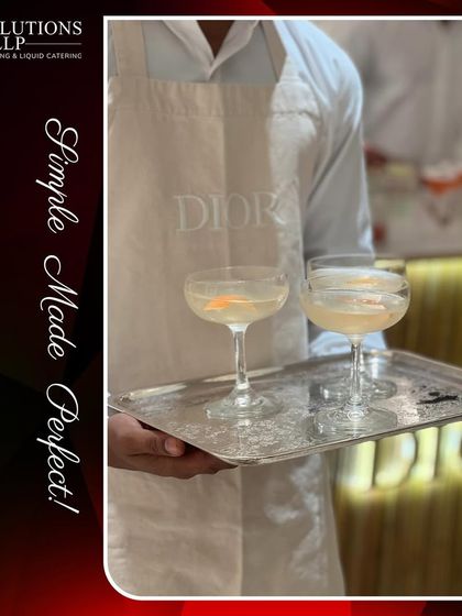 A server in a custom DIOR apron presenting elegant cocktails on a silver tray, showcasing our attention to detail.