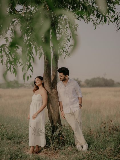 A relaxed portrait of the couple leaning against a tree in a wide-open field, capturing a moment of peaceful connection.