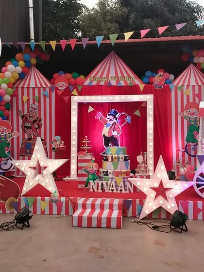 The carnival stage is set with a lit-up central frame, circus tent backdrops, and large star-shaped marquee lights.