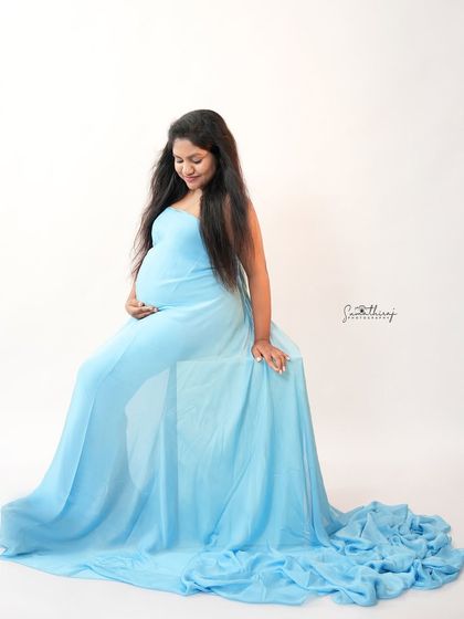 A serene portrait of a mother-to-be in a light blue gown. The simple white background and her gentle smile create a peaceful and classic maternity image.