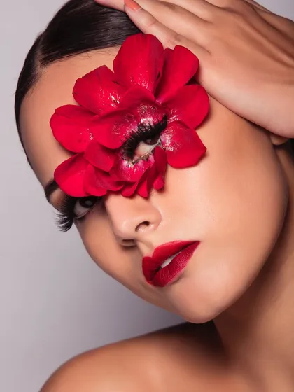 A classic glamour look with a bold red lip and dramatic lashes, made even more striking with a large red flower over one eye.