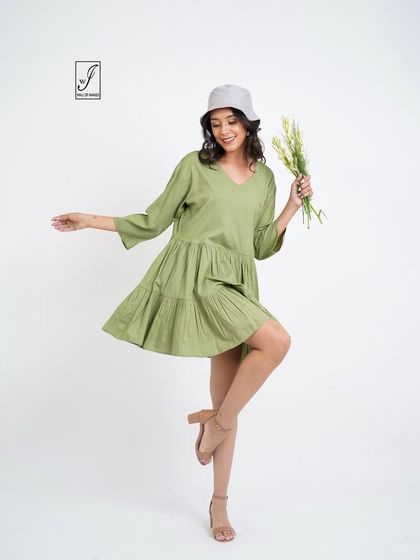 Another playful pose in the same green dress, styled with a bucket hat and flowers.