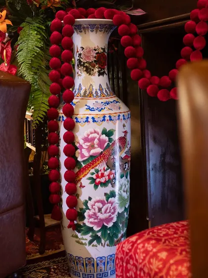A close-up detail of a hand-painted ceramic vase, a classic element that adds an authentic, artisanal touch to the decor. The red velvet garland provides a simple yet luxurious accent.
