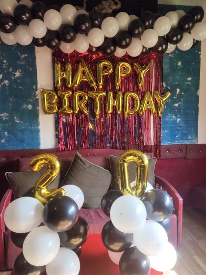 A 20th birthday party with a black, white, and gold theme, including foil numbers and a balloon garland.