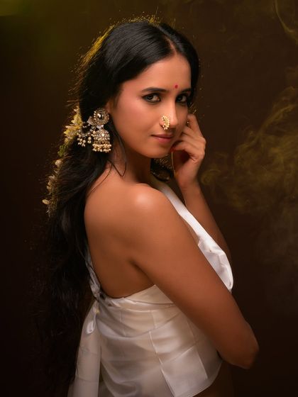 A classic ethnic portrait with a focus on traditional jewelry. The warm lighting and rich brown background create a painterly effect, emphasizing the model's serene beauty.
