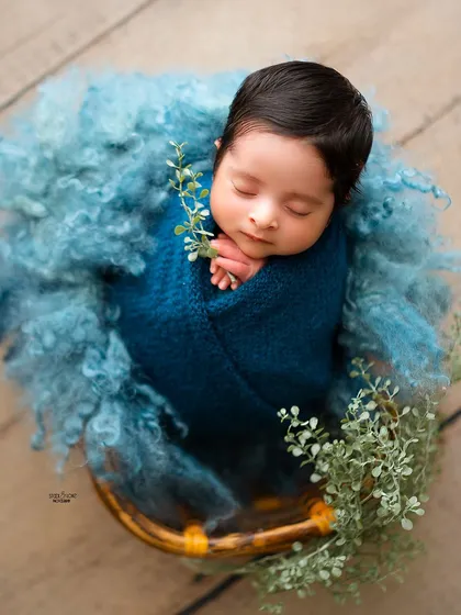 Simple, natural, and oh-so-sweet. This newborn is wrapped in a deep blue swaddle, with just a touch of greenery to create a peaceful, organic feel.