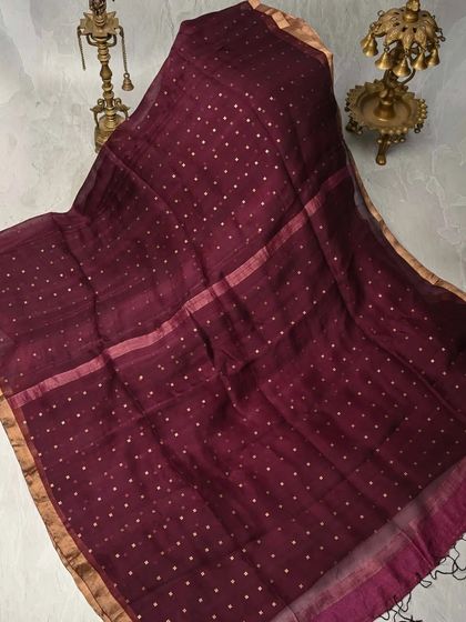 A deep maroon Muslin silk saree with delicate gold butis. The fabric is exceptionally fine and breathable, offering a look of understated luxury.