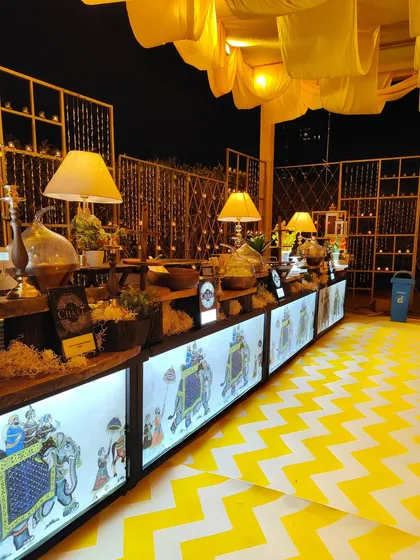 A creative catering station with an illuminated front panel featuring traditional Indian artwork. I pay attention to every detail, including how the food is presented, to enhance the overall theme.