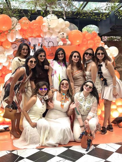 The mom-to-be and her friends posing in front of the vibrant orange backdrop. The dress code and decor came together perfectly for this stylish Hermès-themed celebration.