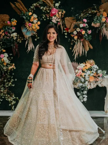 A full-length portrait of Sejal at her reception. Her beautiful ivory lehenga and radiant smile are set against a stunning floral backdrop.