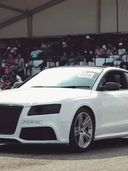 A pristine white Audi S5 waits at the starting line, engine ready to roar. The packed grandstands in the background are a testament to the massive crowd we draw for every race.