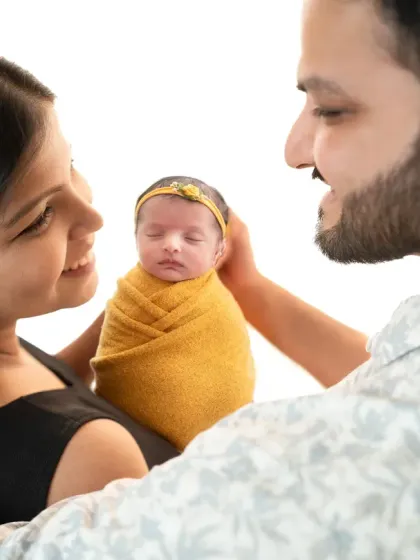 A close-up shot capturing the parents' adoring gaze at their newborn. The baby, wrapped snugly, is the center of their world in this heartwarming family portrait.