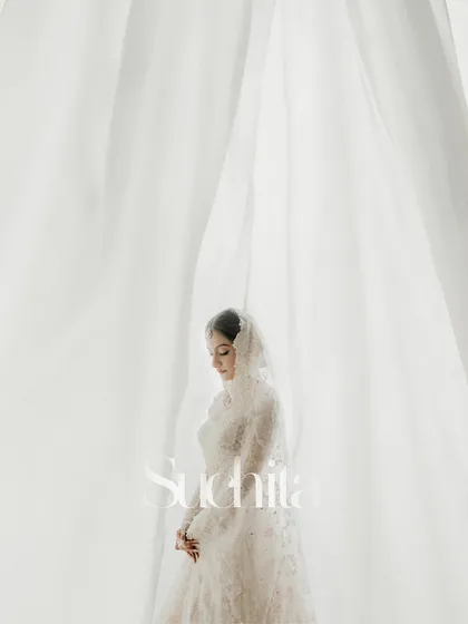 A beautiful, ethereal portrait of the bride, Suchita. The soft white curtains create a dreamy, light-filled backdrop that perfectly complements her delicate white lehenga.