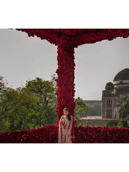 A stunning portrait of the bride, Nandini, framed by a massive arch of red roses, with Humayun's Tomb in the background. It's a truly epic and iconic bridal shot.