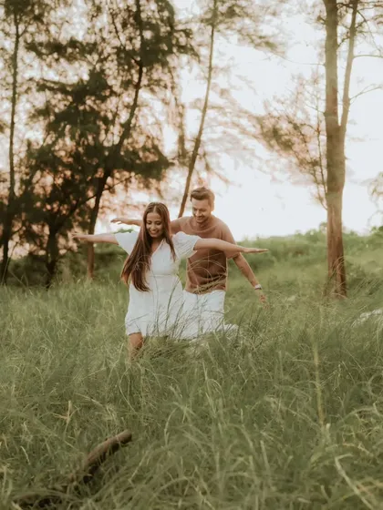 A playful, carefree moment as a couple runs through a field of tall grass with their arms outstretched. This candid photo is full of life, energy, and happiness.