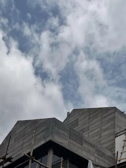 The strong geometry of a roofline under construction. Even in its unfinished state, the architectural form makes a statement against the cloudy sky.