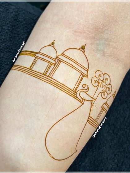 The initial sketch of a peacock and palace design on the arm. This is the first step in creating a detailed and traditional henna piece.