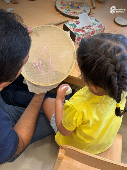 A parent and child work together on an embroidery project. These shared activities strengthen bonds and create opportunities for connection, modeling the patience and collaboration we hope to foster in children.