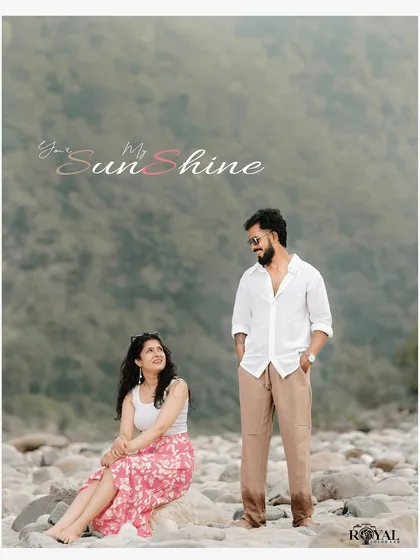 A sweet portrait of a couple on the rocky riverbank, with the man standing and the woman sitting, looking up at him lovingly.
