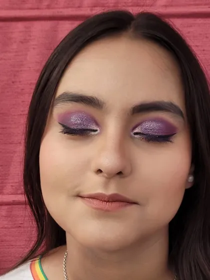 A close-up of a semi cut crease eye makeup look. The vibrant purple is blended with a touch of shimmer on the lid to make the eyes pop, defined by a clean winged liner.