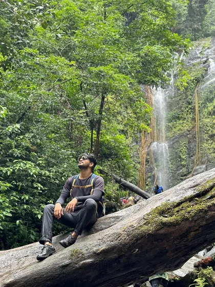 A trekker sits on a fallen log, contemplating the beauty of Hidlumane Falls.