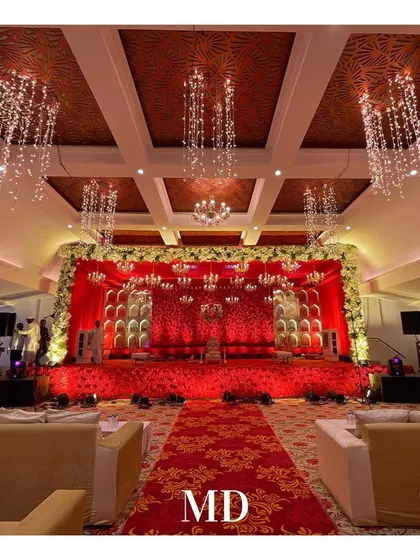The main stage for a red-themed engagement. The backdrop is a wall of red flowers with alcove details, and the ceiling is adorned with cascading crystal chandeliers, creating a luxurious and romantic atmosphere.